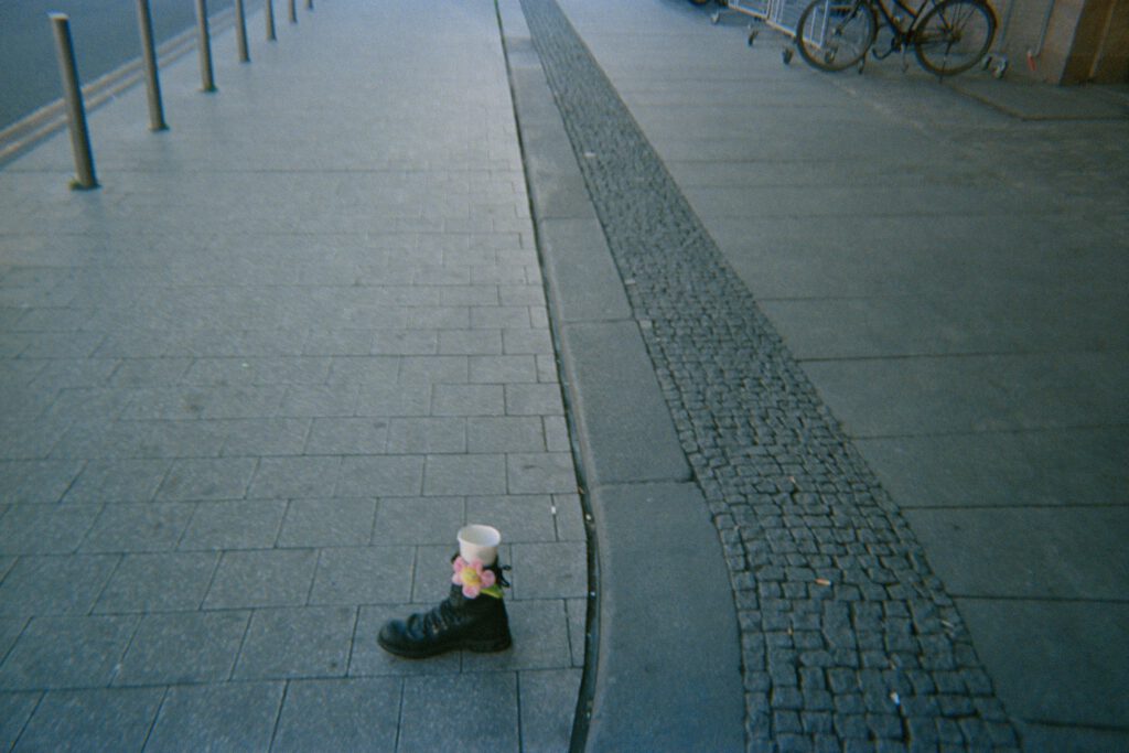Ein Stiefel steht auf dem Boden und in Ihm eine Blume und ein Becher.